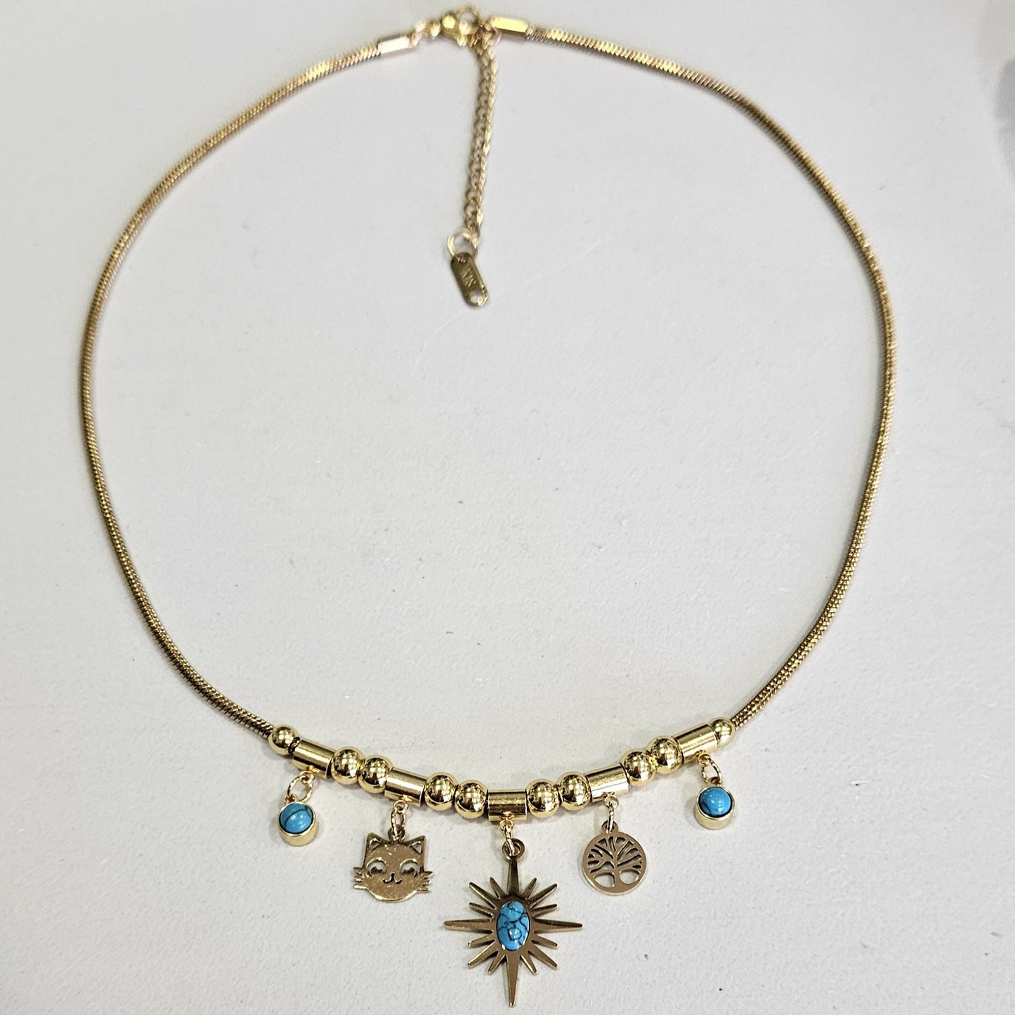 Collar de acero en color dorado con colgantes turquesas y cara de gatito