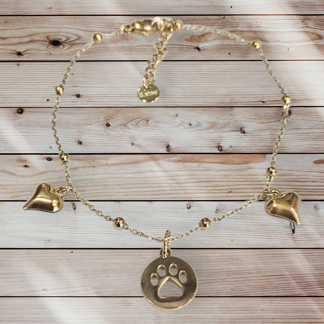 Tobillera de acero en color dorado con abalorio de huella y corazones